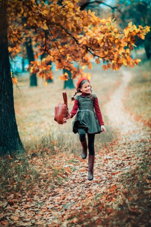 Téléchargez les photos : Portrait d'automne d'une belle jeune écolière en béret rouge et poils tressés avec cartable. Sensibilité enfant positif avec sourire lumineux profiter de la nature dans le parc. - en image libre de droit