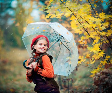 Photo for Autumn portrait of a beautiful young schoolgirl in red beret and braid hairs with umbrella and leaves on it. Tenderness positive child with bright smile enjoying nature in park. - Royalty Free Image
