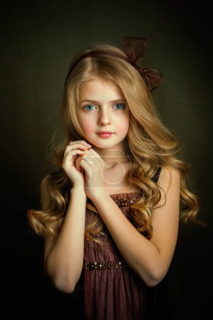 Close up Portrait of a Beautiful blonde girl with blue eyes in vintage dress  .Pretty child with shiny curly hair posing in studio on dark background.