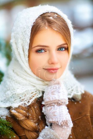 Photo for Winter portrait of a beautiful young girl with long braid hair, blue eyes and knitted lacy scarf standing on a background of wooden and snowflakes. - Royalty Free Image