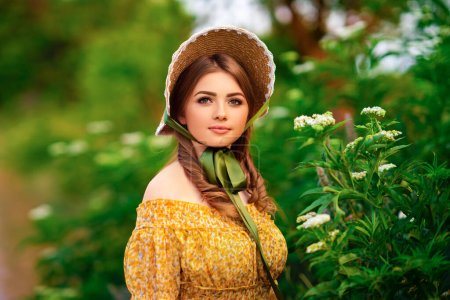 Photo for Pretty young curly girl in straw hat and vintage yellow dress standing near white flowers. Elegant lady walking in countryside.Art work of romantic tenderness model. - Royalty Free Image