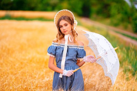 Photo for Pretty young curly girl in straw hat and vintage yellow dress standing in a wheat field. Elegant lady walking in countryside.Art work of romantic tenderness model. - Royalty Free Image