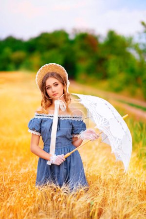 Téléchargez les photos : Jolie jeune fille bouclée en chapeau de paille et robe jaune vintage debout dans un champ de blé. Dame élégante marchant dans la campagne.Oeuvre d'art de modèle de tendresse romantique. - en image libre de droit