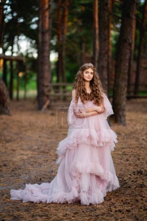 Foto de Hermosa chica con el pelo largo en vestido largo glamour posando en el bosque. Cálida obra de arte de cuento de hadas - Imagen libre de derechos