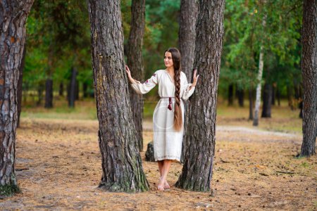 Beautiful extra long braided hair girl in Ukrainian traditional dress posing in forest . Portrait of young attractive stylish woman on colorful warm background.