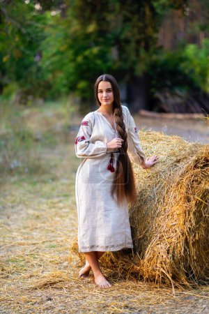 Photo for Beautiful extra long braided hair girl in Ukrainian traditional dress posing on a farm . Portrait of young attractive stylish woman on colorful warm background. - Royalty Free Image
