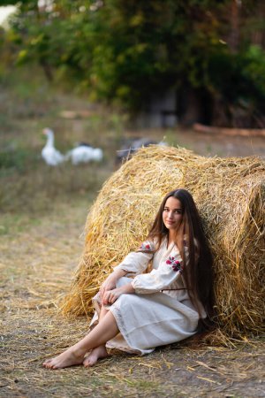 Foto de Hermosa chica de pelo trenzado extra largo en vestido tradicional ucraniano posando en una granja. Retrato de mujer elegante atractiva joven sobre fondo cálido colorido. - Imagen libre de derechos