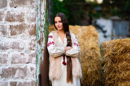 Beautiful extra long braided hair girl in Ukrainian traditional dress posing on a farm . Portrait of young attractive stylish woman on colorful warm background.