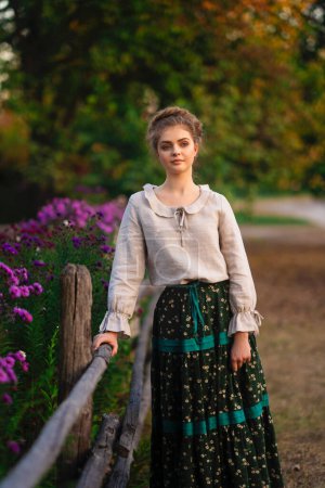 Foto de Hermosa chica trenzada rubia en vestido largo rural posando en un pueblo. Bastante joven modelo en campo arte foto. - Imagen libre de derechos