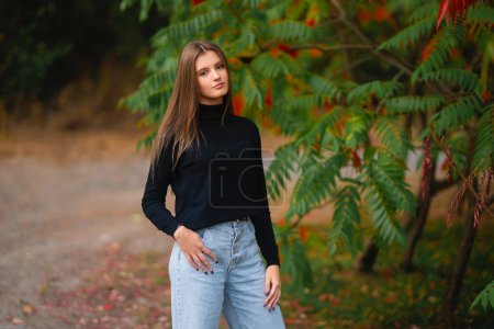 Téléchargez les photos : Belle fille en jeans et golf noir jouissant de la nature en plein air. Jeune joli modèle posant sur fond vert. - en image libre de droit