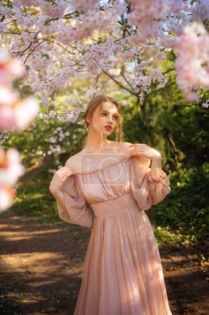 Belle fille en robe vintage rose debout près de fleurs colorées. Oeuvre d'art de femme romantique. Jolie modèle de tendresse posant dans le parc de fleurs.