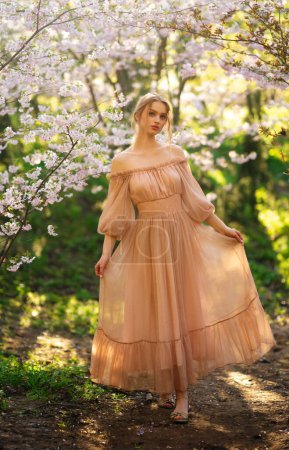 Belle fille en robe vintage rose debout près de fleurs colorées. Oeuvre d'art de femme romantique. Jolie modèle de tendresse posant dans le parc de fleurs.