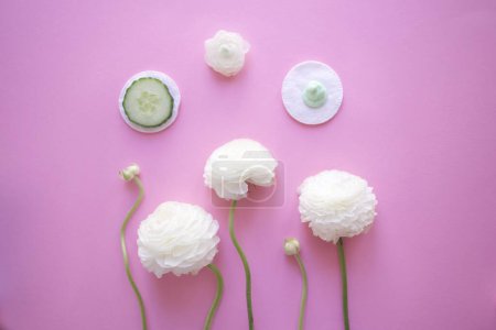 Téléchargez les photos : Ranunculus and on cotton pads a slice of cucumber and cream on a pink background top view - en image libre de droit