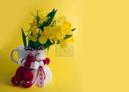 Bouquet of yellow daffodils tied with red-white martenitsa, martisor on yellow background copy space