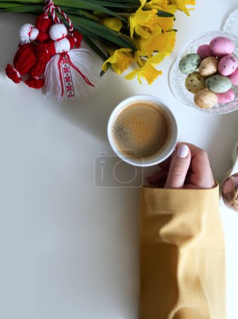 Bouquet of daffodils with red and white martenitsa and a womans hand holding a cup of coffee
