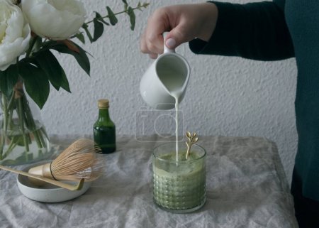 Téléchargez les photos : Une main de femme verse du lait dans une tasse de thé vert matcha. Photo de haute qualité - en image libre de droit