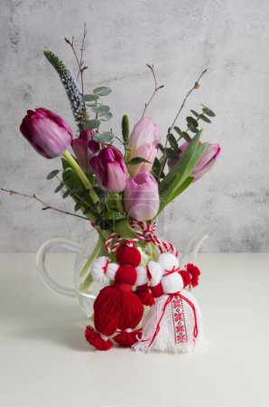Bouquet de tulipes roses et violettes nouées à la martenitsa rouge-blanc, martiseur sur une table blanche close up