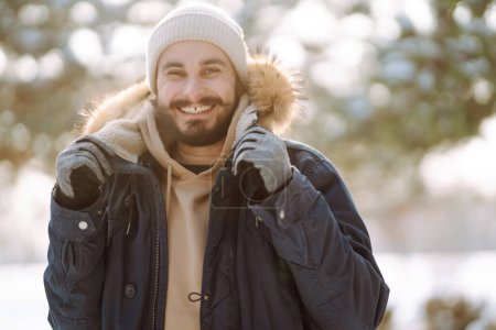 Téléchargez les photos : Homme barbu souriant à la caméra dans le parc d'hiver. Saison, Noël, voyage et concept de personnes. - en image libre de droit