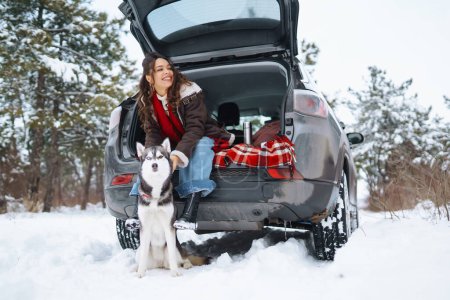 Téléchargez les photos : Jeune femme et chien husky mignon profitant à l'extérieur dans la voiture. Concept de voyage. Saison d'hiver. - en image libre de droit