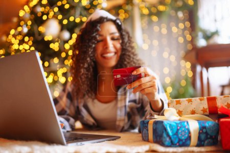Photo for Young woman with credit card, gifts, and laptop. Online shopping at Christmas holidays. - Royalty Free Image
