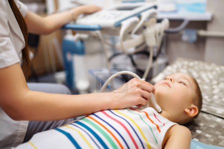 Kleiner Junge unterzieht sich einer Schilddrüsen-Ultraschalluntersuchung Der Arzt untersucht die Kehle des Kindes in einer Klinik mit moderner Ausrüstung. Gesundheitskonzept