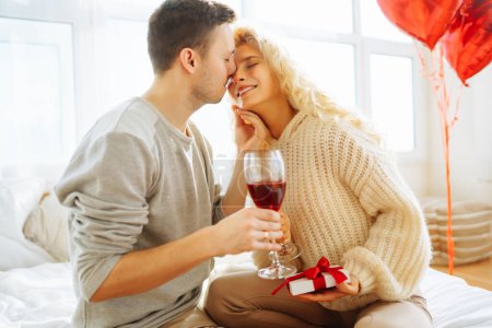 Photo for Young couple at home celebrating Valentine's Day  with glass of red wine. Romantic day together. Relationship, surprise and love concept. - Royalty Free Image