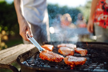 Téléchargez les photos : Entreprise de personnes réunies pour barbecue dans le jardin d'été. Amis griller la viande, amusez-vous, détendez-vous. acceptation du mode de vie, vacances, week-ends. Pique-nique et barbecue. - en image libre de droit