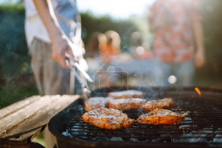 Photo for Ompany of people gathered for barbecue in summer garden. Friends grill meat, have fun, relax. oncept of lifestyle, holidays, weekends. Picnic and barbecue. - Royalty Free Image