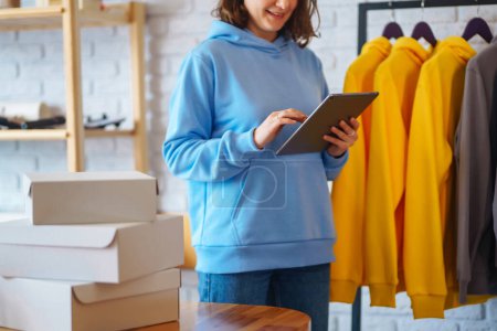 Porträt einer Inhaberin eines Modegeschäfts, die ein digitales Tablet benutzt, um den Warenbestand in einem Bekleidungsgeschäft auf Schienen zu überprüfen. Online-Verkauf. Einkaufskonzept.