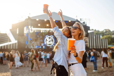 Fröhlich unterhalten sich zwei junge Freundinnen auf der Beachparty mit Bier. Glücklich genießen zwei Frauen das Wochenende beim Musikfest. Das Konzept von Freundschaft, Urlaub, Wochenende.