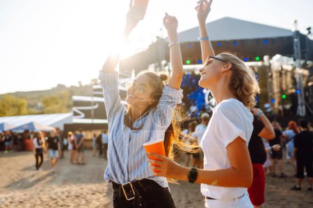 Fröhlich unterhalten sich zwei junge Freundinnen auf der Beachparty mit Bier. Glücklich genießen zwei Frauen das Wochenende beim Musikfest. Das Konzept von Freundschaft, Urlaub, Wochenende.