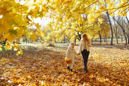 Feliz madre e hija se divierten en el parque de otoño al atardecer. Elegante madre e hija disfrutan del parque de otoño. Familia en un paseo. Infancia, caminatas, descanso.