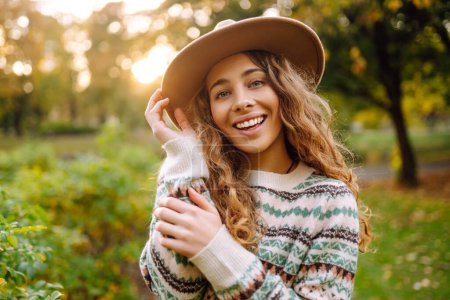 Photo for Portrait of a stylish curly woman in a hat, enjoys the autumn weather in a sunny park. oncept of fashion, style. Outdoor recreation. - Royalty Free Image