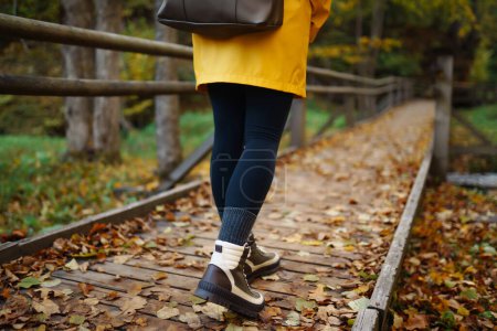 Téléchargez les photos : Les pieds des femmes en bottes longent un sentier de randonnée en bois dans la forêt d'automne. Concept de voyage vacances, sentier de randonnée - en image libre de droit