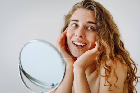 Téléchargez les photos : Belle femme à la peau problématique travaille dans son petit miroir. La cosmétologie. Concept de soins de la peau. - en image libre de droit