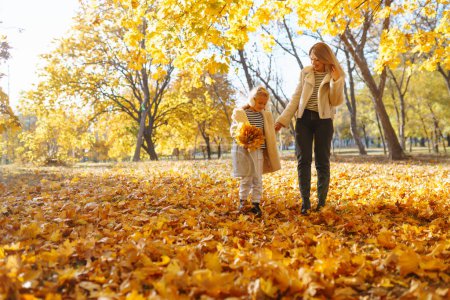 Kleine Tochter und ihre Mutter mit herbstgelbem Laub amüsieren sich im Herbst gemeinsam im Stadtpark. Kindheitskonzept, Spaziergänge, Wochenenden.