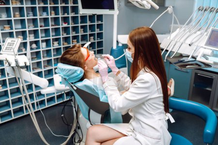 Téléchargez les photos : Jeune femme dans le fauteuil du dentiste pendant une intervention dentaire. Santé dentaire. Femme heureuse avec un beau sourire à un rendez-vous chez le dentiste. Médecine, concept de santé. - en image libre de droit