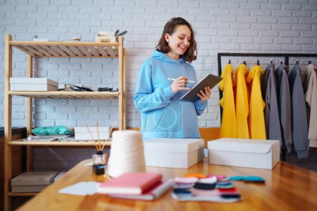 Clothing store: young woman blogger,  small business owner, seller using tablet checks and packs orders of online store, e-commerce. Online Shopping Cart notion.