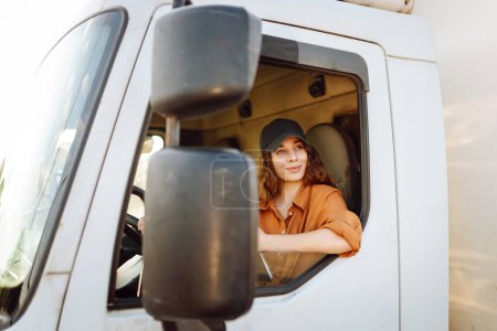 Foto de Una mujer joven se sienta en la cabina de un camión de carga. Tema Industria del transporte. - Imagen libre de derechos