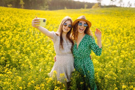 Zwei Frauen machen ein Selfie beim Spazierengehen auf einem blühenden Feld. Mode, Schönheitskonzept. Sommerlandschaft.