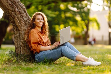 Foto de Mujer bonita con portátil en la hierba verde. Educación en línea. Informática, trabajo remoto. Negocios, blogs, concepto freelance. - Imagen libre de derechos