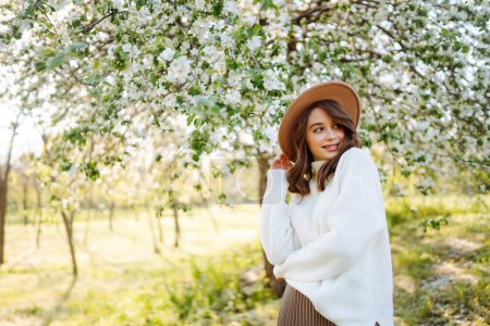Mujer joven se encuentra cerca de un árbol en flor en un parque de primavera. El concepto de juventud, amor, moda, turismo y estilo de vida.