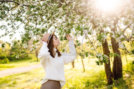 Eine junge Frau steht neben einem blühenden Baum in einem Frühlingspark. Das Konzept von Jugend, Liebe, Mode, Tourismus und Lifestyle.