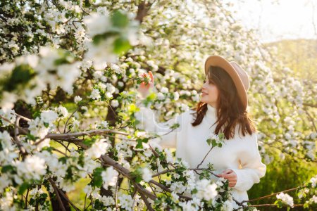 Young woman stands near a blossoming tree in a spring park. The concept of youth, love, fashion, tourism and lifestyle.