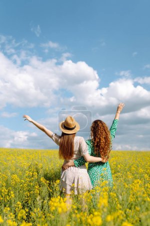 Zwei junge Frauen in einem schönen Feld mit gelben Blumen. Sie springen und haben Spaß. Tag der Freundschaft
