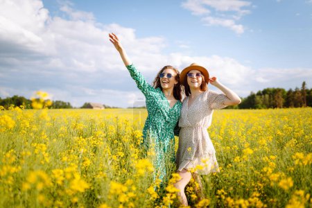 Dos mujeres jóvenes en un hermoso campo con flores amarillas. Saltan y se divierten. Día de la amistad