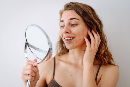 Portrait d'une jeune fille avec une peau problématique se regarde dans le miroir. Boutons sur le visage. Soins du visage. Problème d'acné.