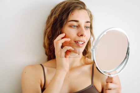 Retrato de una joven con problemas de piel se ve en el espejo. Espinillas en la cara. Cuidado facial de la piel. Problema del acné.