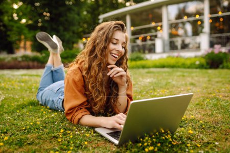 Téléchargez les photos : Femme heureuse avec les cheveux bouclés avec un ordinateur portable en plein air. Formation en ligne, travail indépendant, concept technologique. - en image libre de droit