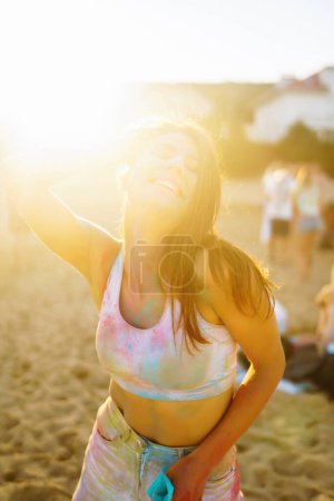 Téléchargez les photos : Femme heureuse couverte de poudre colorée arc-en-ciel célébrant holi festival de couleur. Jeune femme s'amusant avec de la poudre colorée à l'extérieur. Fête à la plage. Vacances traditionnelles indiennes. - en image libre de droit